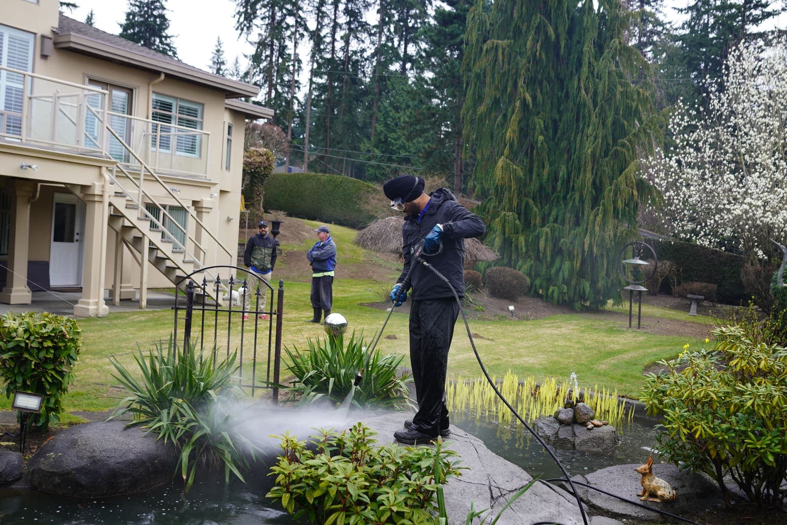 Two-person crew pressure washing a stone patio and walkway behind a large home