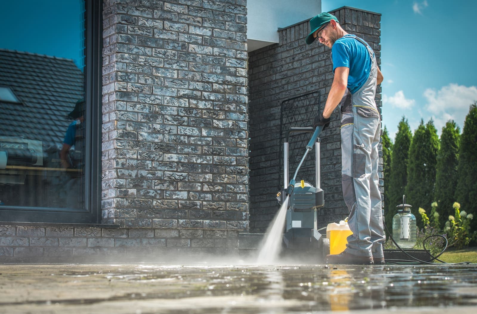 Worker pressure washing a stone-clad wall and patio at a modern home