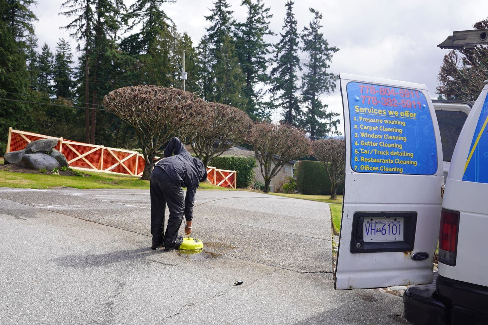 Technician running a surface cleaner on a driveway beside the service van