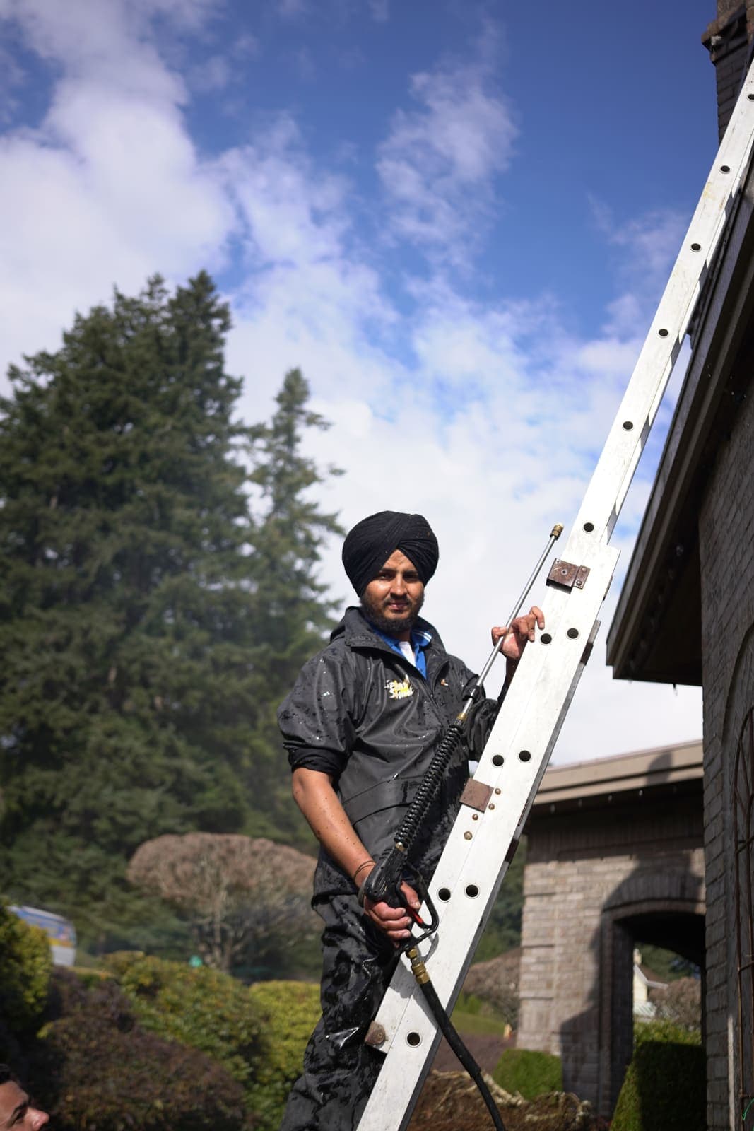 Technician steadying an extension ladder against a brick house