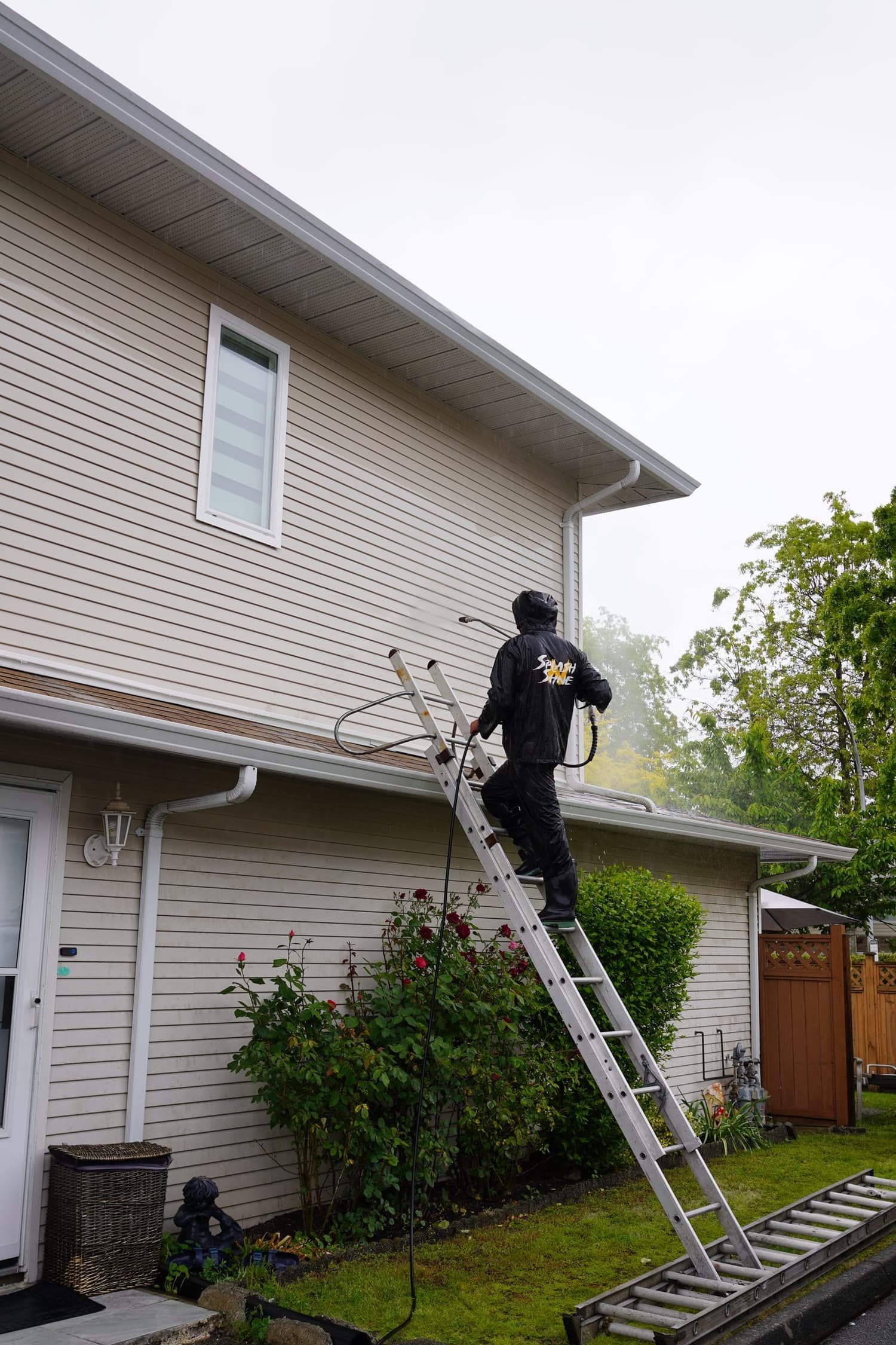 A worker clearing gutters on a home surrounded by heavy tree cover