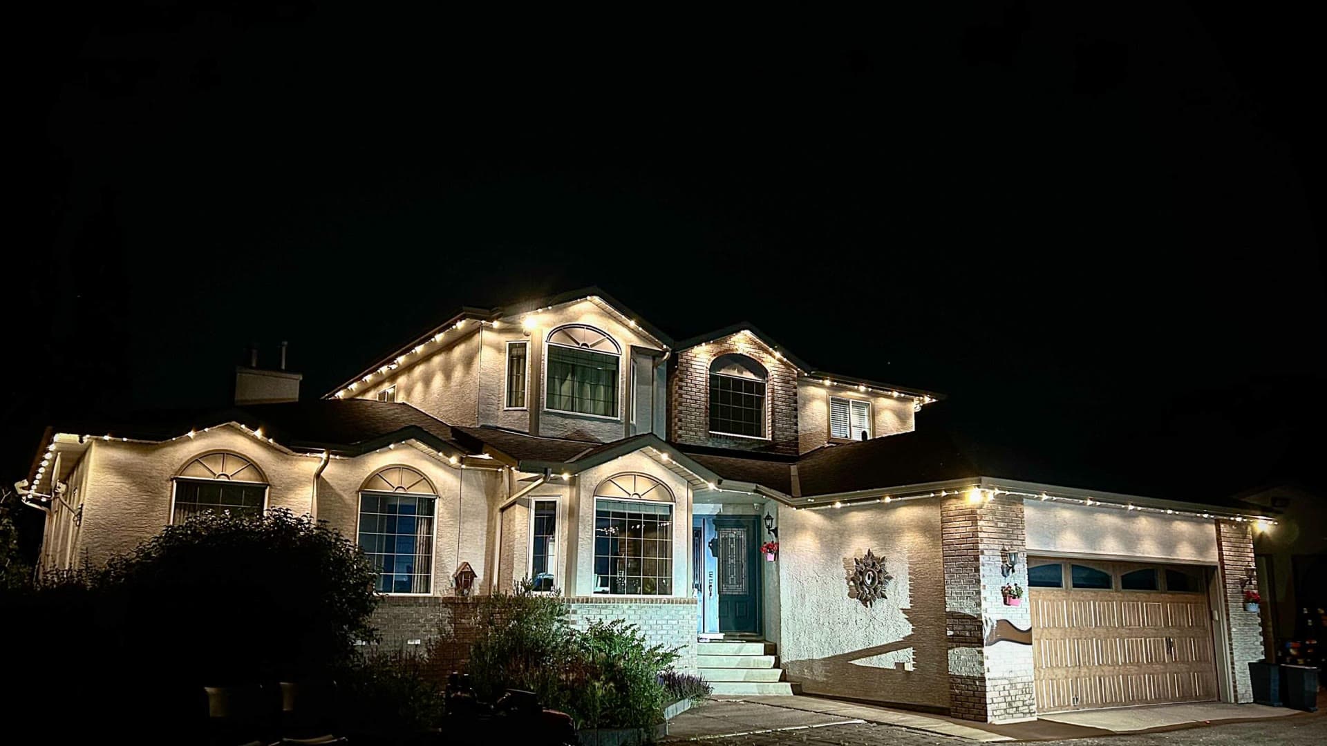 Two-storey home outlined in warm-white permanent holiday lights after dark