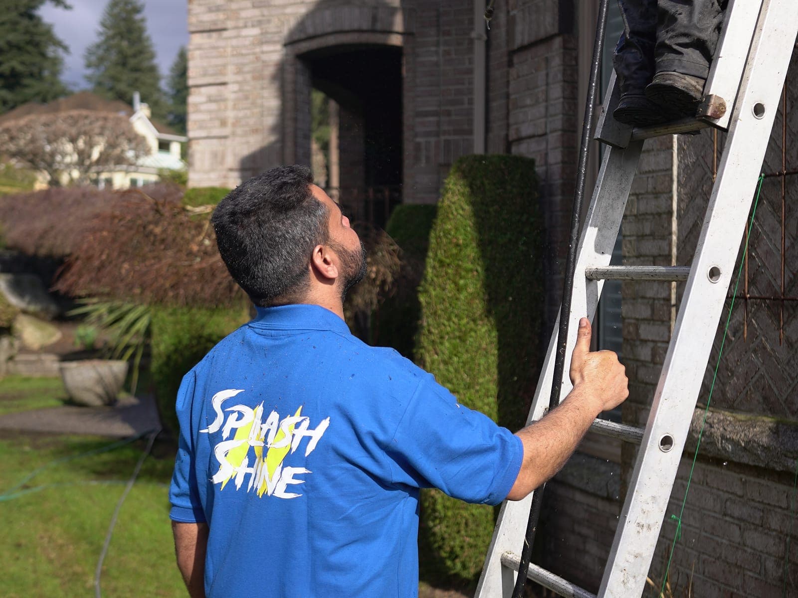 Splash N Shine technician on a ladder clearing the gutter line of a Lower Mainland home