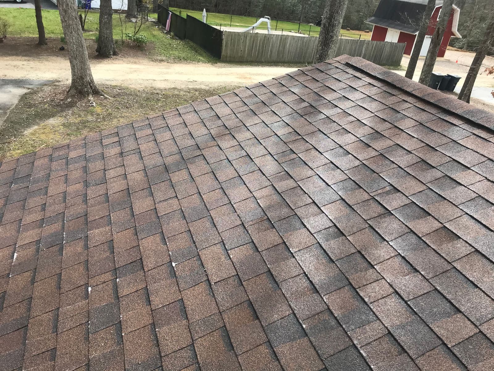 Asphalt shingle roof mid-clean, moss and algae being removed across the slope